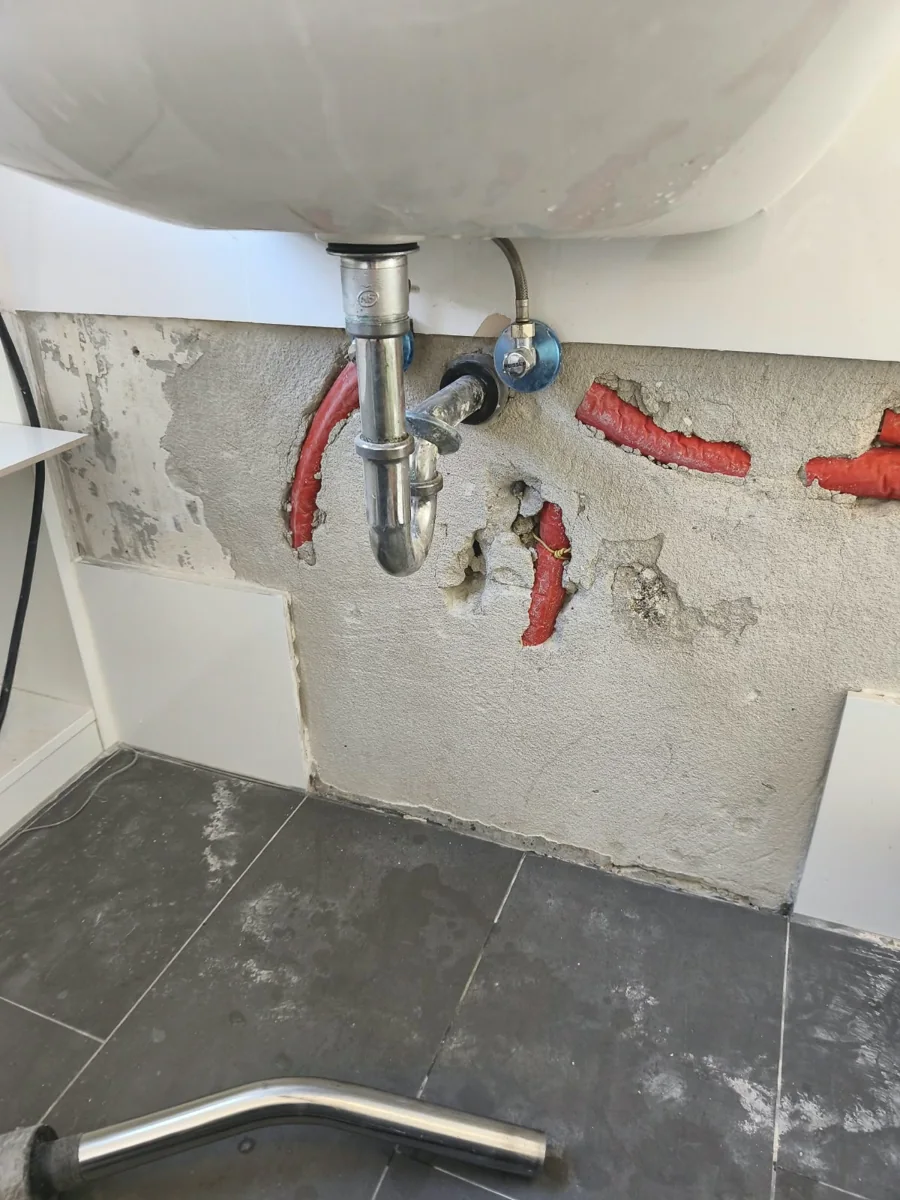 Für Reparaturarbeiten geöffnete Fliesenwand unter einem Waschtisch.